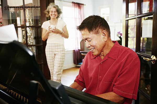 Frau beobachtet Ehemann beim Klavierspielen im Wohnzimmer