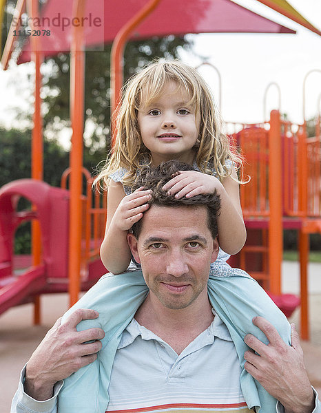 Kaukasischer Vater hält seine Tochter auf dem Spielplatz