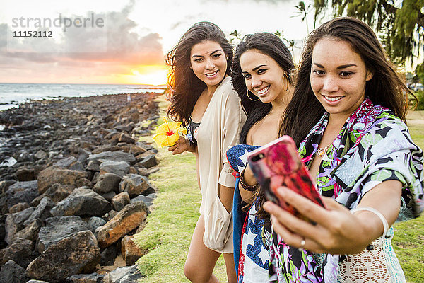 Pazifische Insulanerinnen fotografieren mit ihrem Handy in der Nähe des felsigen Strandes