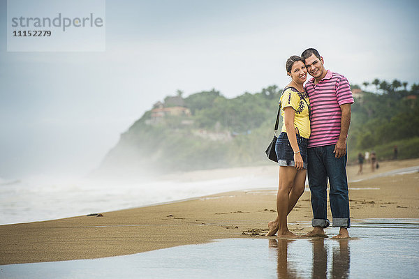 Hispanisches Paar  das sich in den Wellen am Strand umarmt