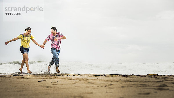 Hispanisches Paar läuft in den Wellen am Strand