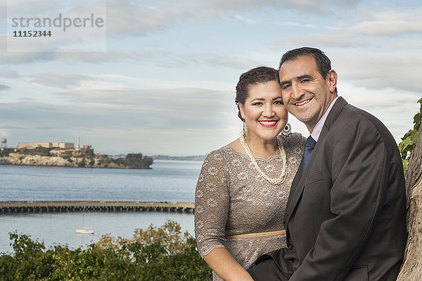Hispanisches Paar in formeller Kleidung lächelt in der Nähe des Ufers