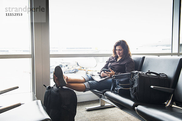 Hispanische Frau  die im Flughafen eine SMS auf ihrem Handy schreibt