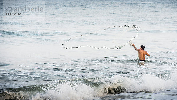 Mann wirft Fischernetz in die Wellen des Ozeans