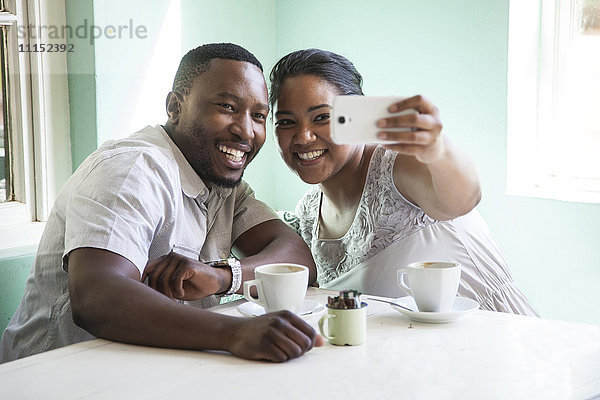 Lächelndes Paar nimmt Handy-Selfie am Tisch