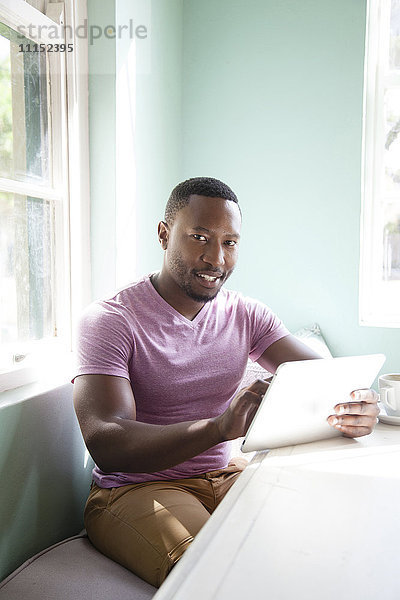 Schwarzer Mann benutzt digitales Tablet am Tisch