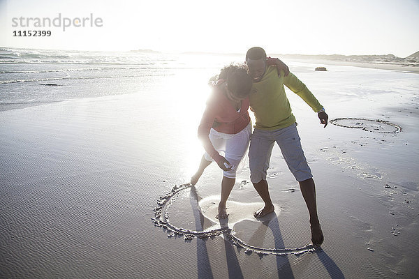 Paar zeichnet Herz in Sand am Strand