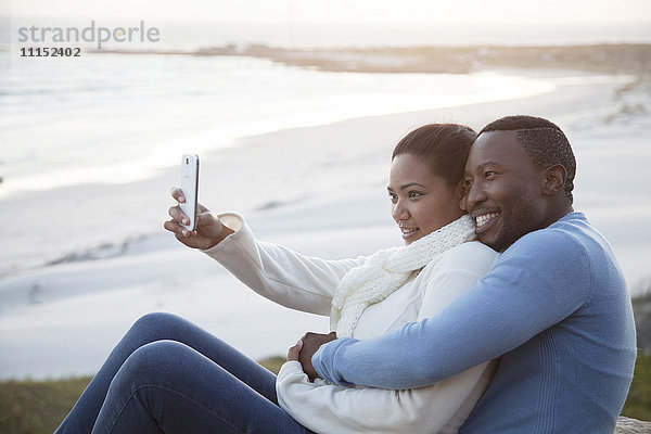 Lächelndes Paar nimmt Handy-Selfie am Strand
