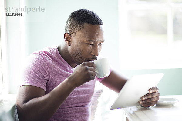 Schwarzer Mann trinkt Kaffee mit digitalem Tablet