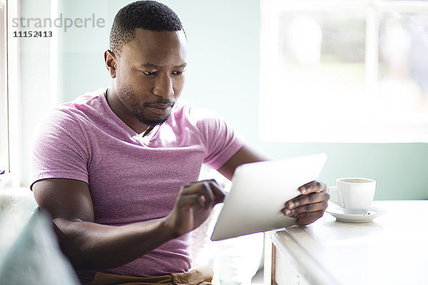 Schwarzer Mann benutzt digitales Tablet beim Frühstück