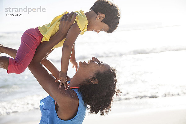 Gemischtrassige Mutter hebt Tochter am Strand