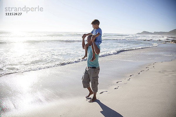Gemischtrassiger Vater trägt Sohn auf den Schultern am Strand