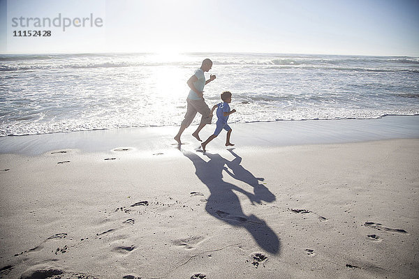 Gemischtrassiger Vater und Sohn laufen am Strand