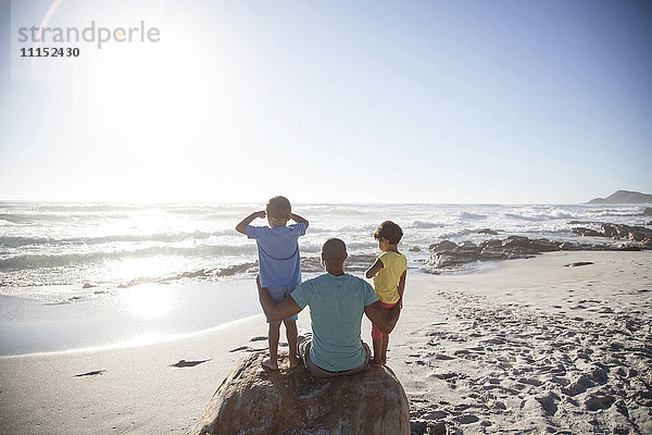 Gemischtrassiger Vater und Kinder sitzen am Strand