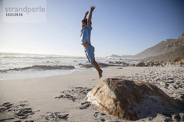 Gemischtrassiger Junge springt von einem Felsen am Strand