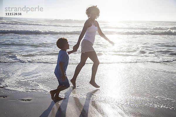 Gemischtrassige Mutter und Sohn spielen in den Wellen am Strand