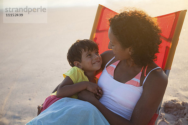 Gemischte Rasse Mutter und Tochter umarmen im Stuhl am Strand