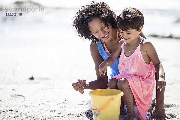 Gemischtrassige Mutter und Tochter spielen am Strand