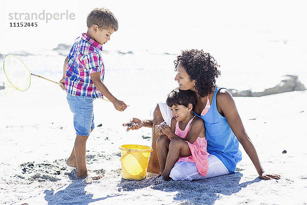 Gemischtrassige Mutter und Kinder spielen am Strand