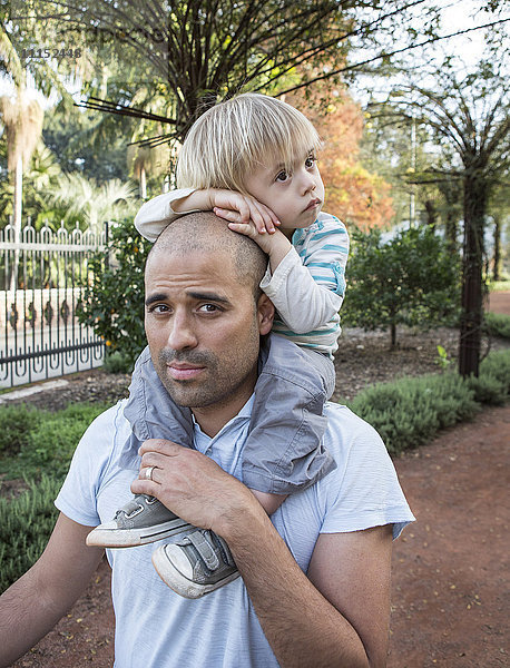 Hispanischer Vater trägt seinen Sohn im Park auf den Schultern