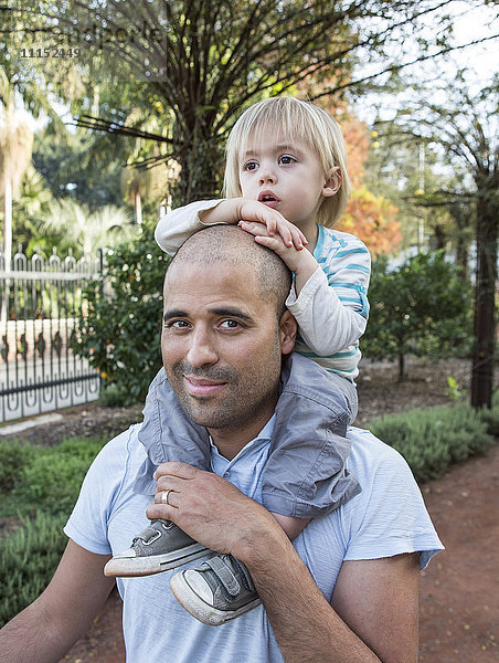 Hispanischer Vater trägt seinen Sohn im Park auf den Schultern