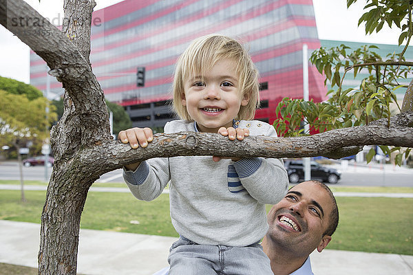 Hispanischer Vater und Sohn spielen auf einem Baum im Park