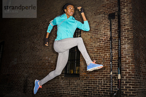 Schwarze Frau springt nachts in der Nähe einer Backsteinmauer