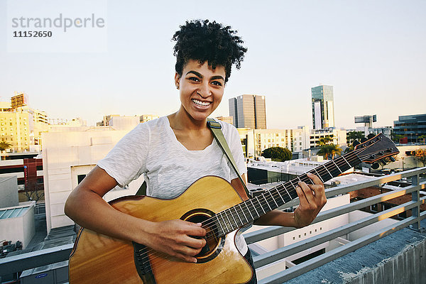 Lächelnde Frau  die auf einem Hausdach Gitarre spielt