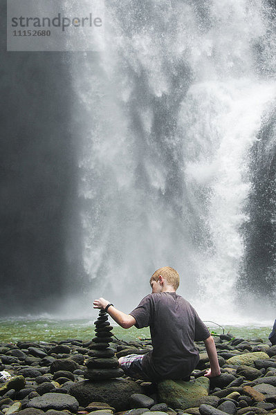 Kaukasischer Junge stapelt Steine in der Nähe eines Wasserfalls