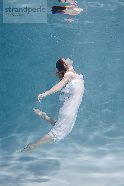 Unterwasseransicht einer kaukasischen Frau im Kleid beim Schwimmen im Pool