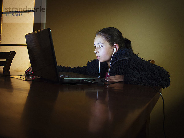 Gemischtrassiges Mädchen  das am Abend am Tisch einen Laptop benutzt