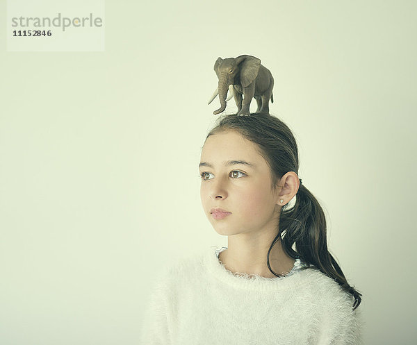 Gemischtrassiges Mädchen hält einen Spielzeugelefanten auf dem Kopf