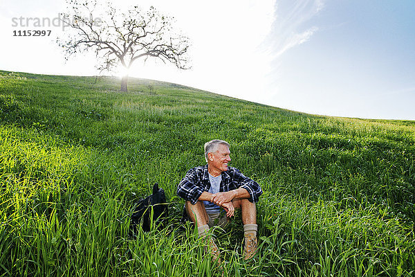 Älterer kaukasischer Mann sitzt auf einem grasbewachsenen Hügel