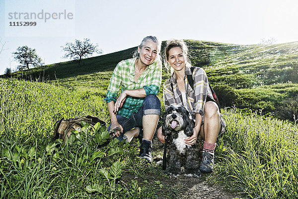 Kaukasische Mutter und Tochter gehen mit ihren Hunden auf einem grasbewachsenen Hügel spazieren