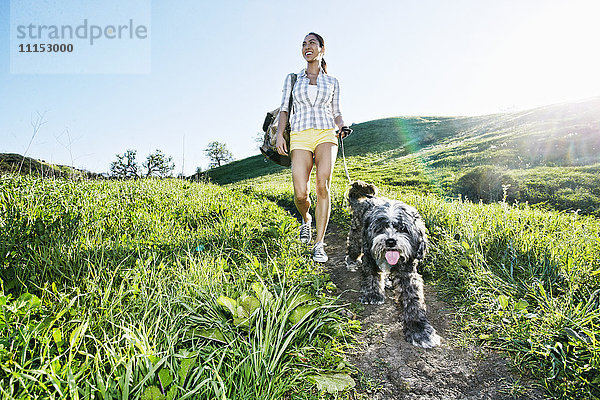 Gemischtrassige Frau geht mit Hund auf grasbewachsenem Hügel spazieren