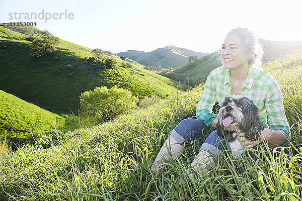 Ältere kaukasische Frau führt Hund auf grasbewachsenem Hügel aus