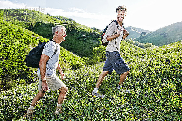 Kaukasischer Vater und Sohn gehen auf einem grasbewachsenen Hügel spazieren