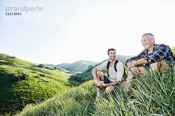 Kaukasischer Vater und Sohn sitzen auf einem grasbewachsenen Hügel