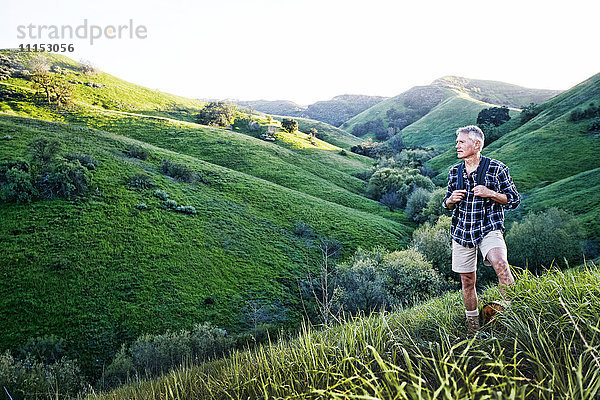 Älterer kaukasischer Mann lächelnd auf grasbewachsenem Hügel