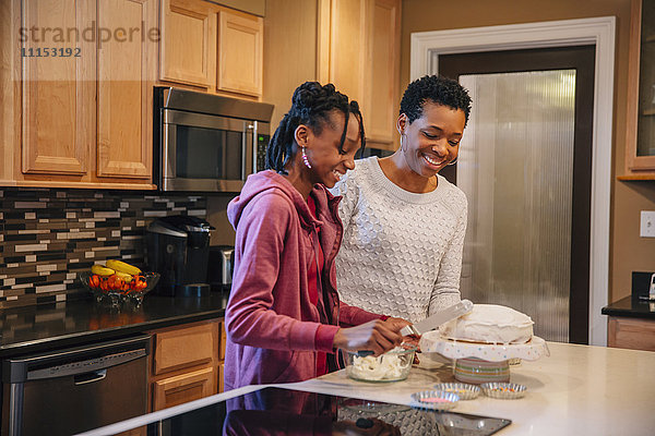 Schwarze Mutter und Tochter dekorieren Kuchen in der Küche