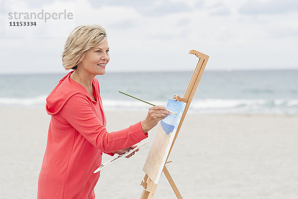 Ältere kaukasische Frau malt am Strand