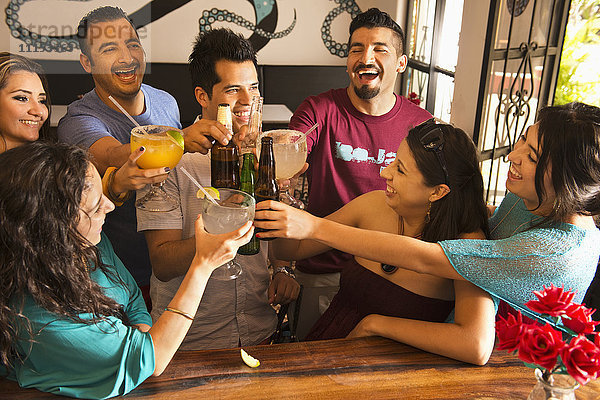 Hispanische Freunde stoßen mit Getränken an der Bar an