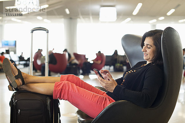 Hispanische Geschäftsfrau benutzt Mobiltelefon im Wartebereich eines Flughafens