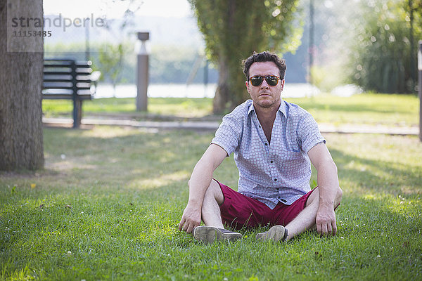 Kaukasischer Mann sitzt im Gras im Park