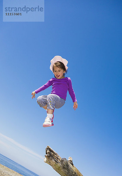 Low angle view of mixed race girl jumping from log on beach