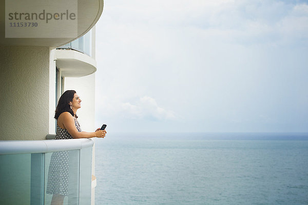 Hispanische Frau bewundert das Meer vom Hotelbalkon aus