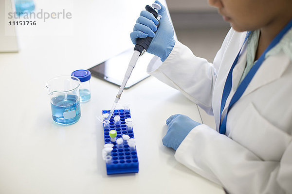 Gemischtrassige Wissenschaftlerin  die im Labor eine Probe in ein Röhrchen pipettiert