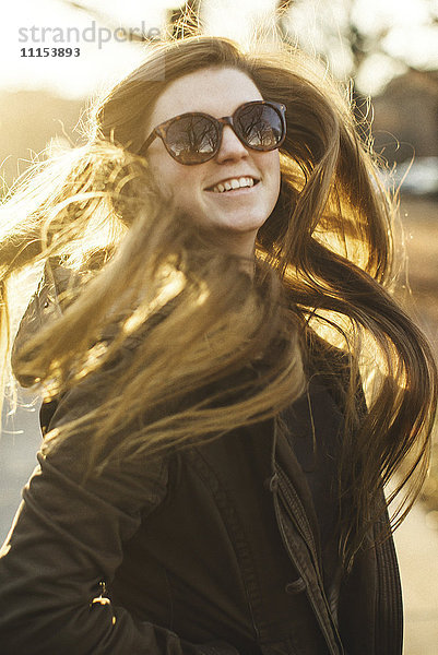 Lächelnde kaukasische Frau  die ihr Haar im Freien wirft