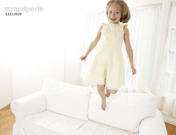 Kaukasisches Mädchen springt auf Sofa im Wohnzimmer
