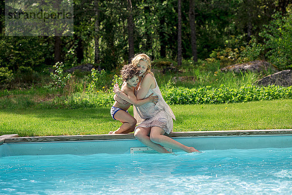 Mutter umarmt Sohn am Swimmingpool im Hinterhof